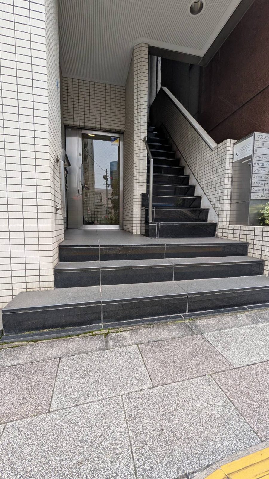 マスマンビルの入口。階段横に手すりがあります。エレベーターで8階へ